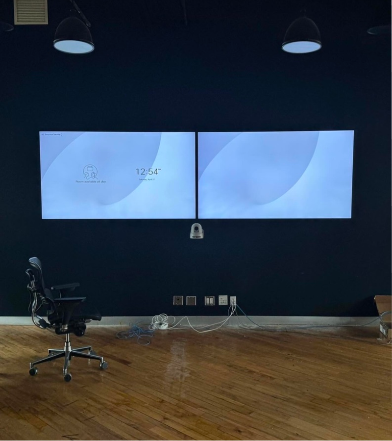 Two TV screen mounted on dark blue wall with office chair on the left side