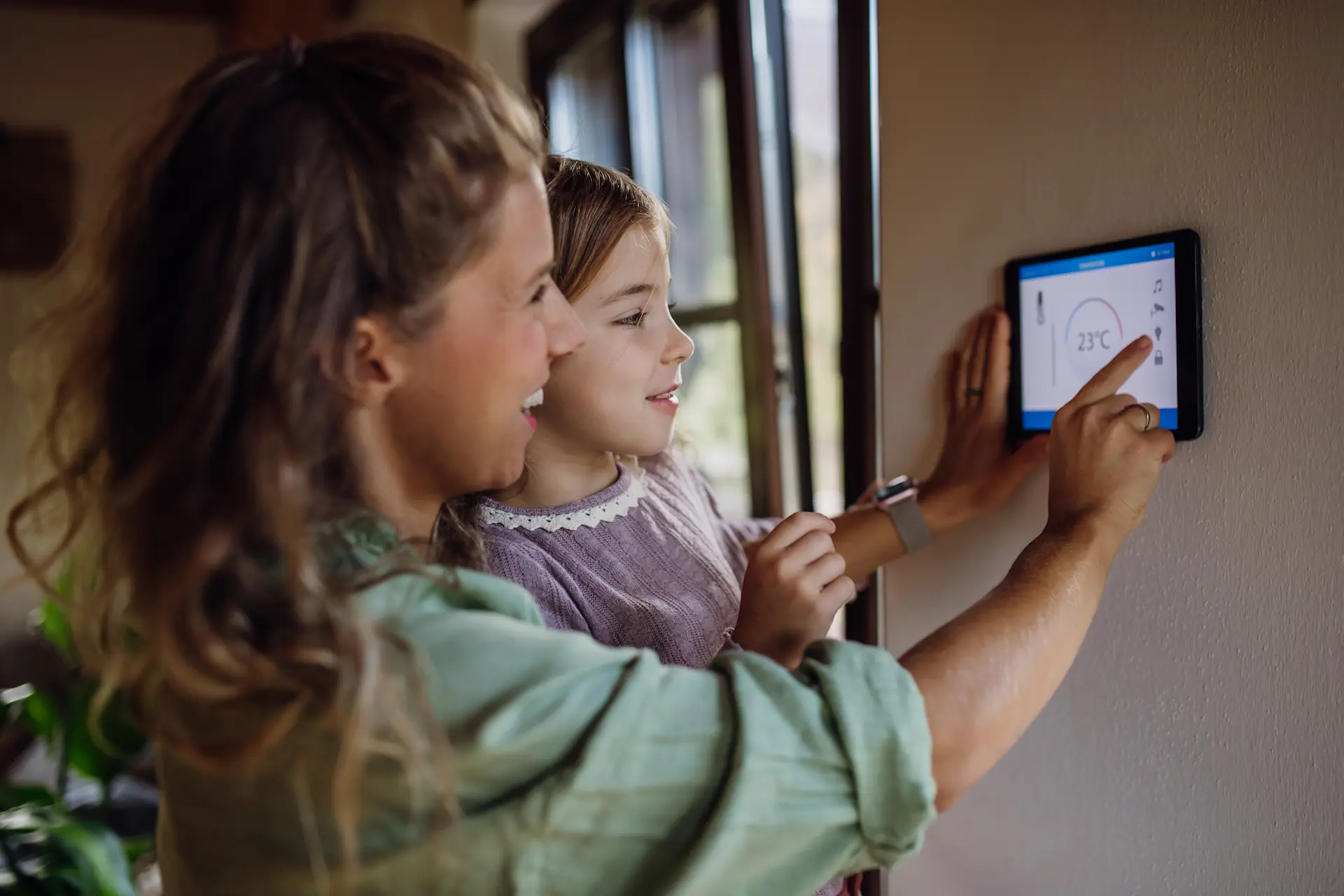 Girl helping mother to adjust, lower heating temperature on thermostat.