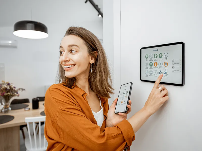 Young woman controlling home with a digital touch screen panel installed on the wall in the living room