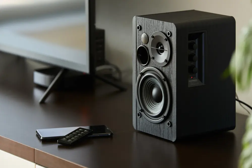 Bookshelf speaker with remote controller and smartphone on a TV stand